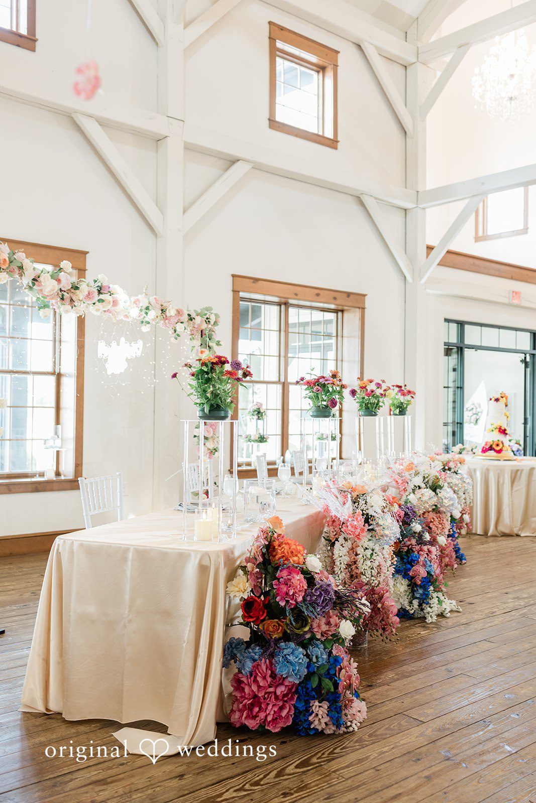 Daniel + Dalte A long table set for a reception with tall floral arrangements and pink chairs in a room with a high ceiling.
