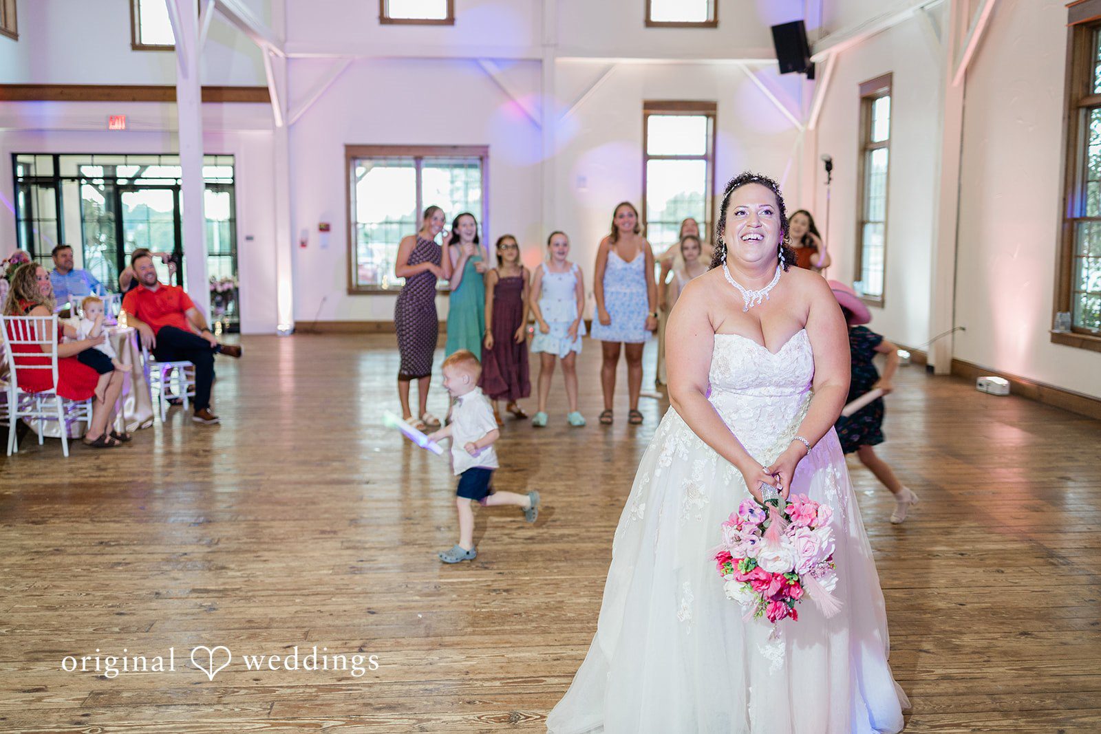 Daniel + Dalte A bride holding a bouquet stands on a dance floor as guests watch in the background.