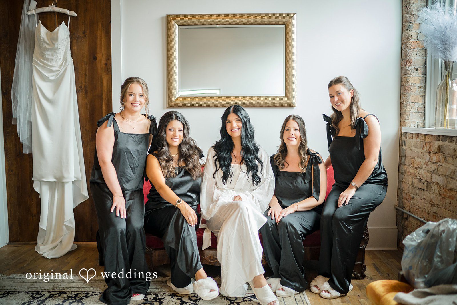 August 01, 2026 – Haley & Austin – (ID-4892) A bride smiling while sitting and posing with her bridesmaids dressed in matching black gowns.