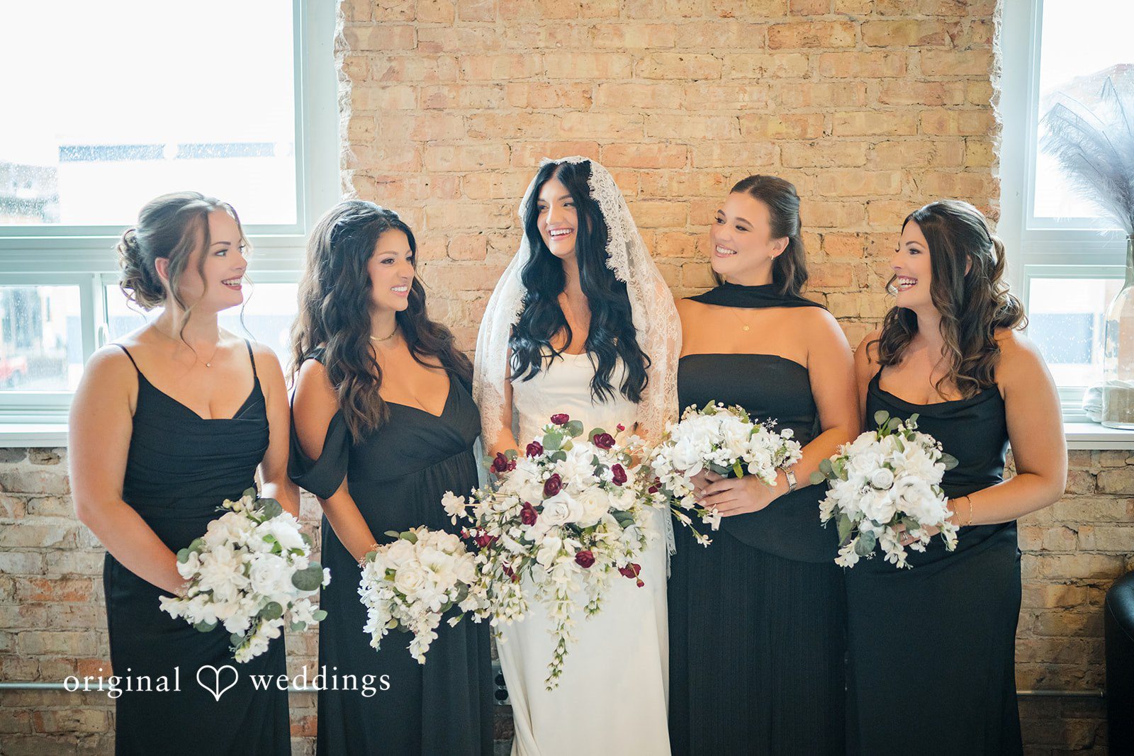 August 01, 2026 – Haley & Austin – (ID-4892) A bride standing and smiling alongside her bridesmaids holding matching white bouquets.