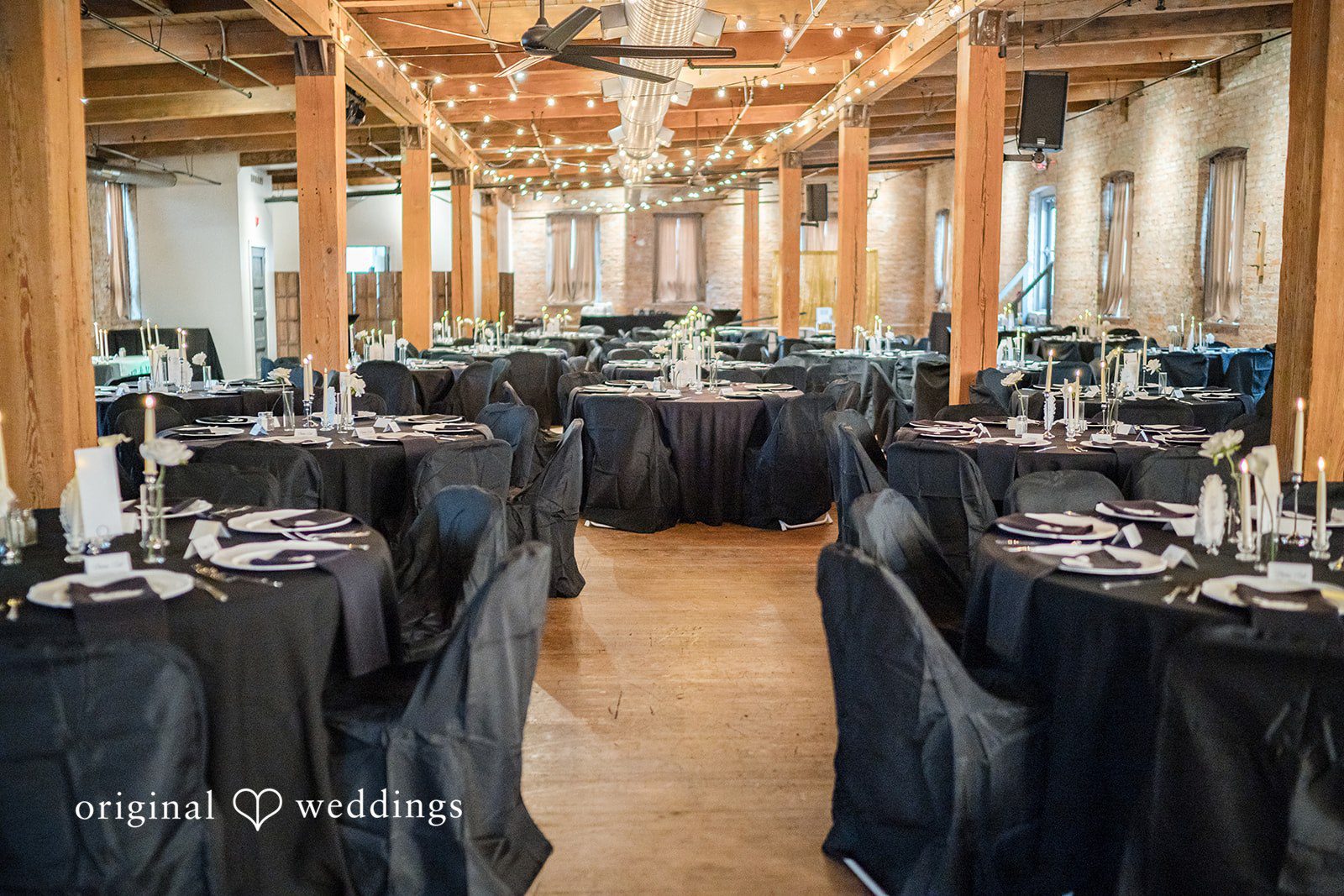 Haley + Austin An elegant wedding reception hall set up with long black tables, dark chairs, and white floral centerpieces.