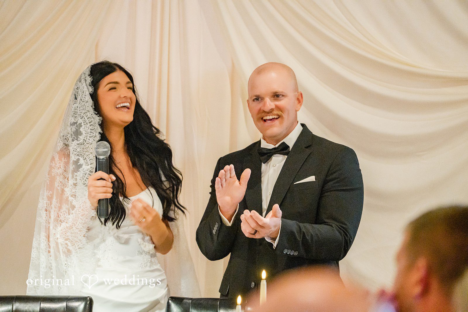 August 01, 2026 – Haley & Austin – (ID-4892) A bride speaking into a microphone while a groom stands beside her clapping and smiling.
