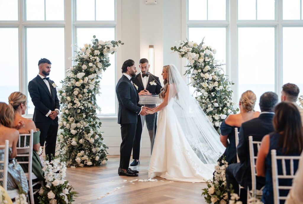 Guests watching the bride arrive at the floral arch, captured by Boston wedding photographers from Original Weddings at The Wychmere
