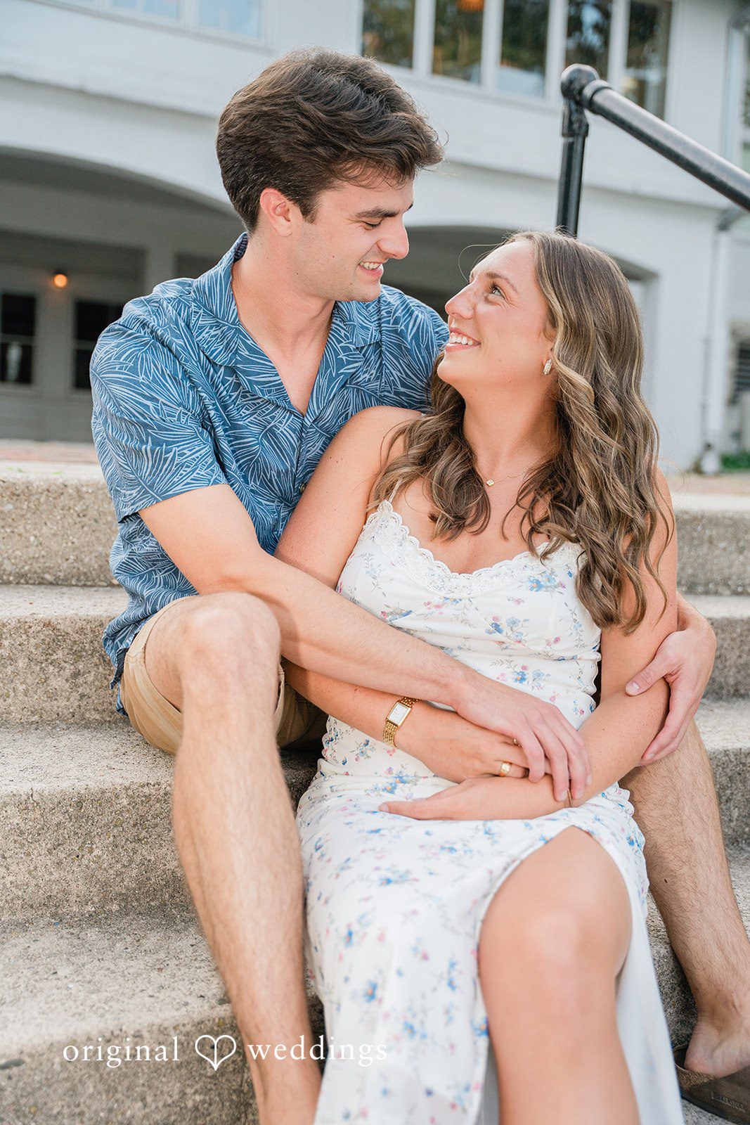 A couple sitting together on stone steps, smiling at each other.