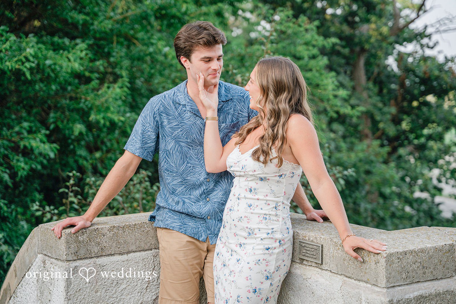 A couple standing close together smiling next to a stone railing.