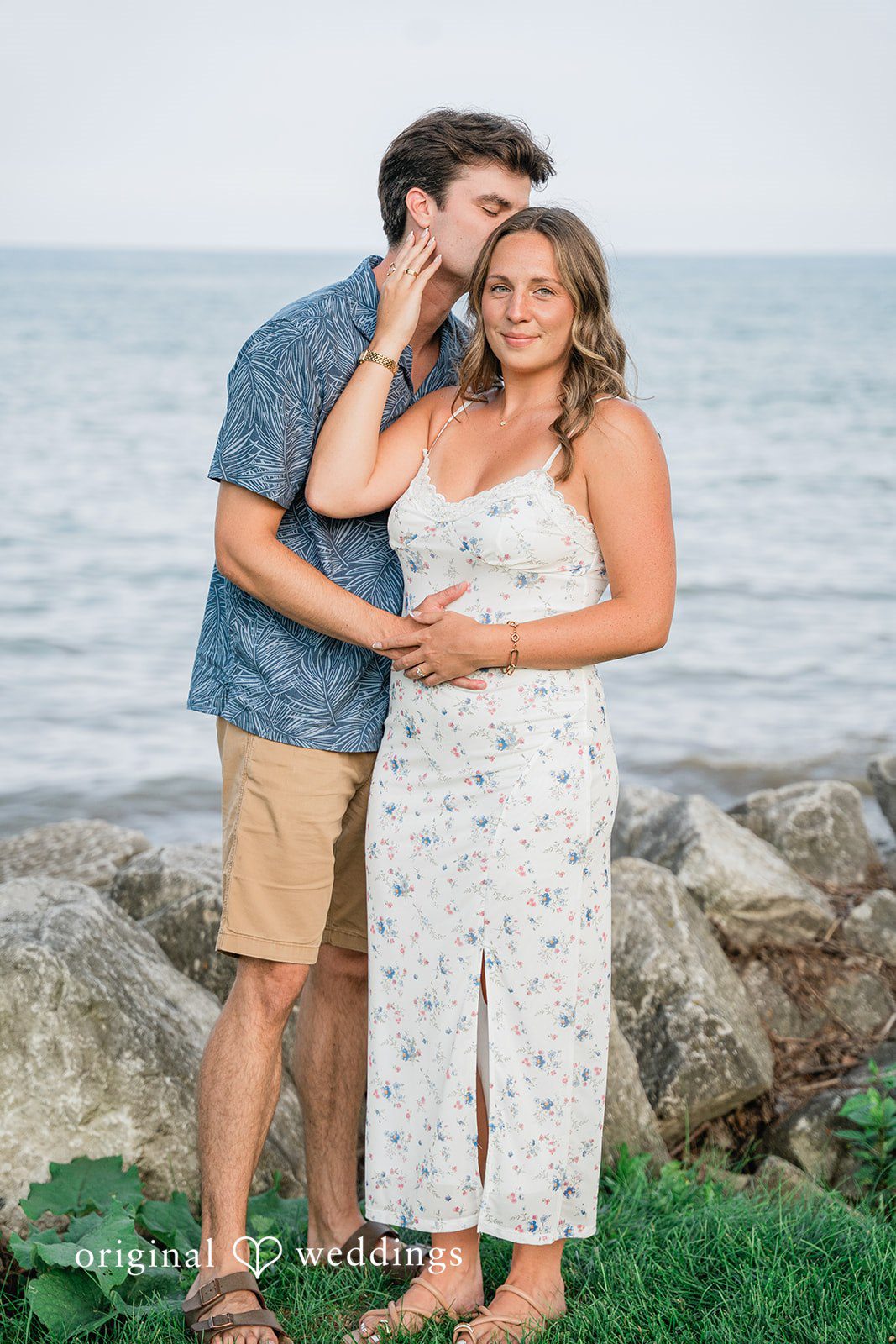A couple holding each other close while standing on a rocky beach.
