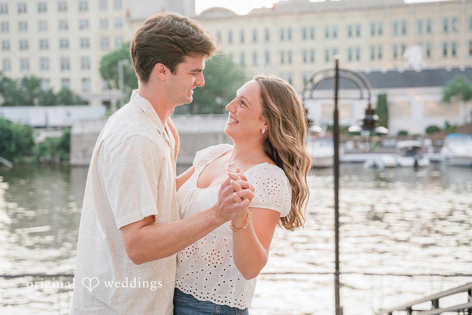 Couple hold hands and smile at each other in a city setting.