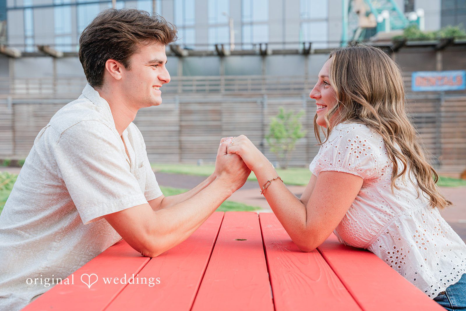 A couple sitting across from each other at a red picnic table.