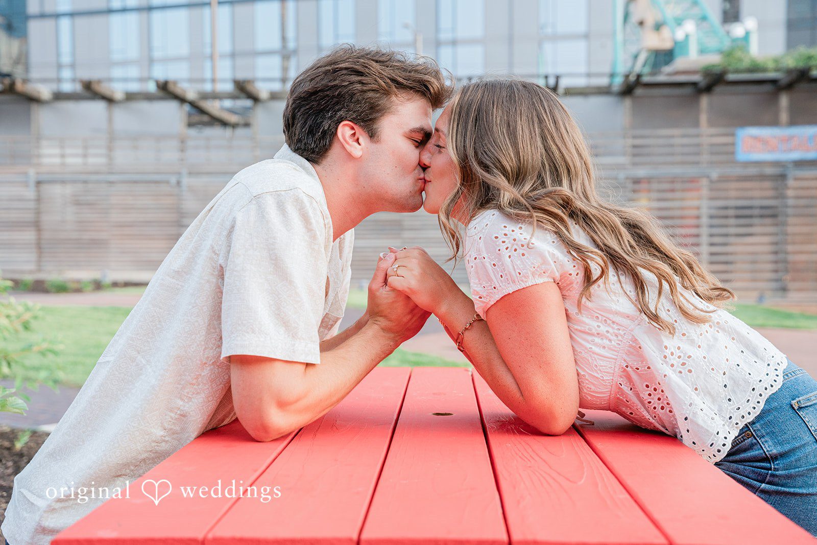 A couple leaning across a red picnic table to share a close moment.