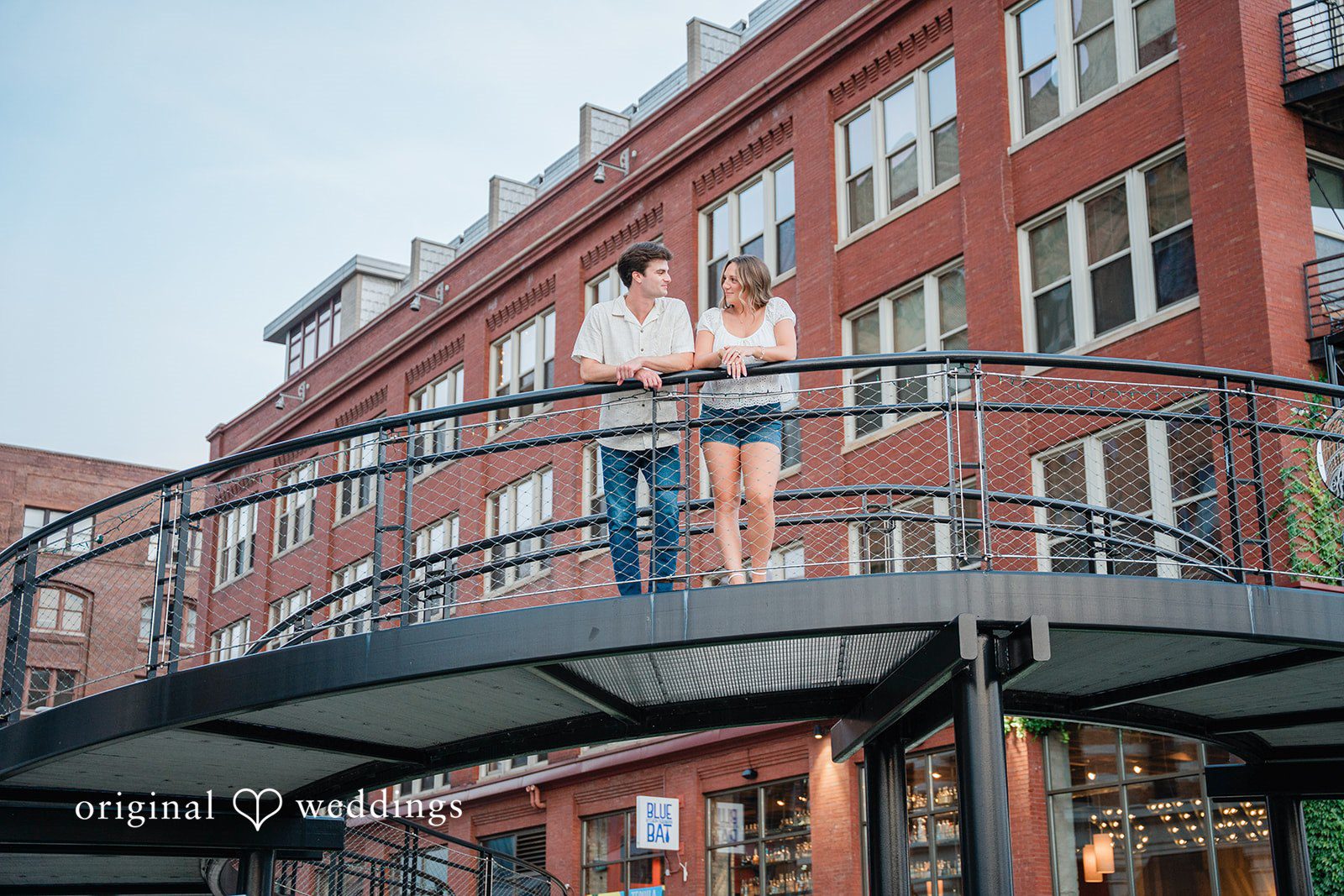 A couple standing together on an elevated metal walkway near a brick building.