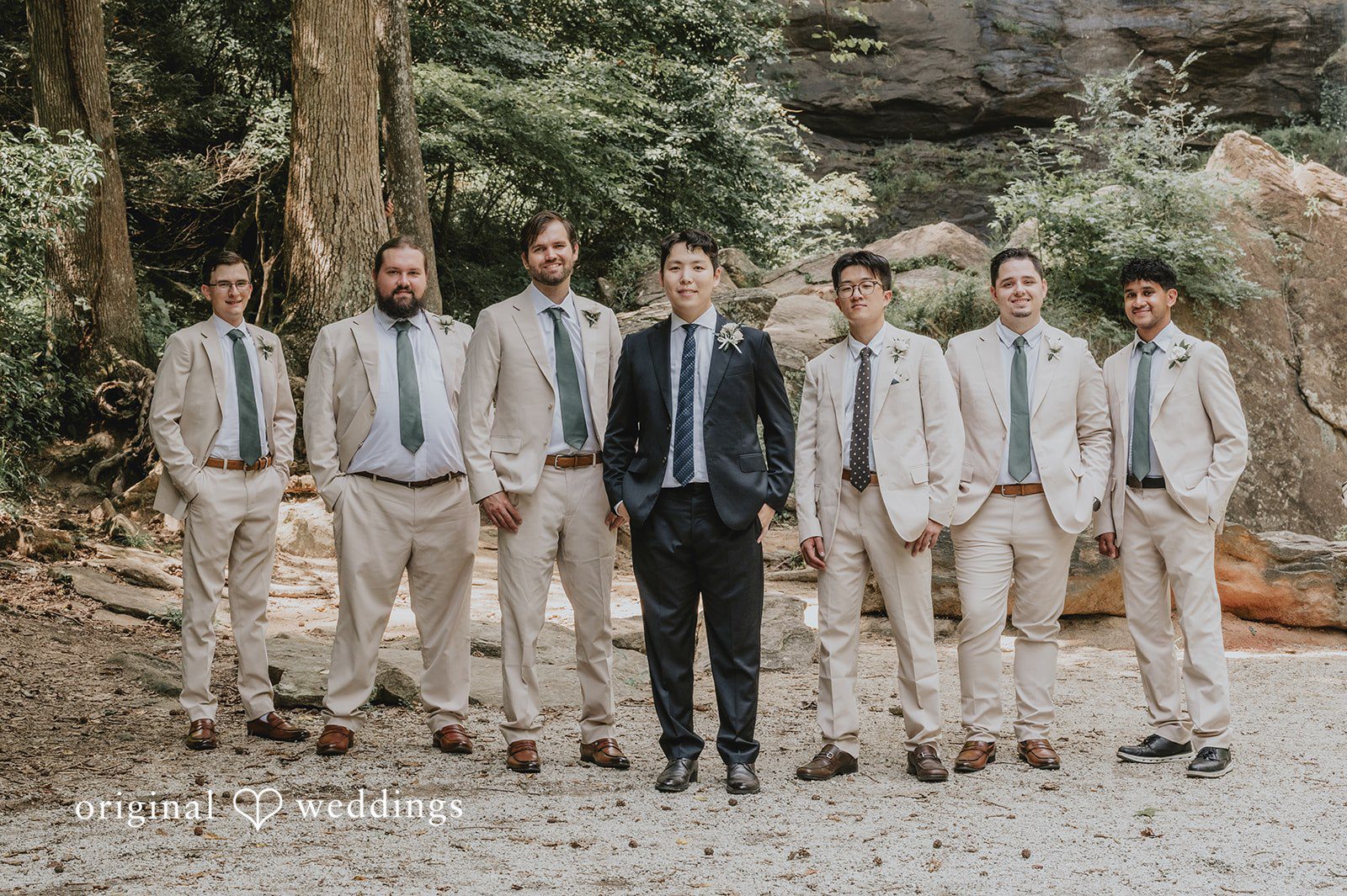 Sean + Hannah A line of groomsmen in light-colored suits stand side-by-side outdoors.