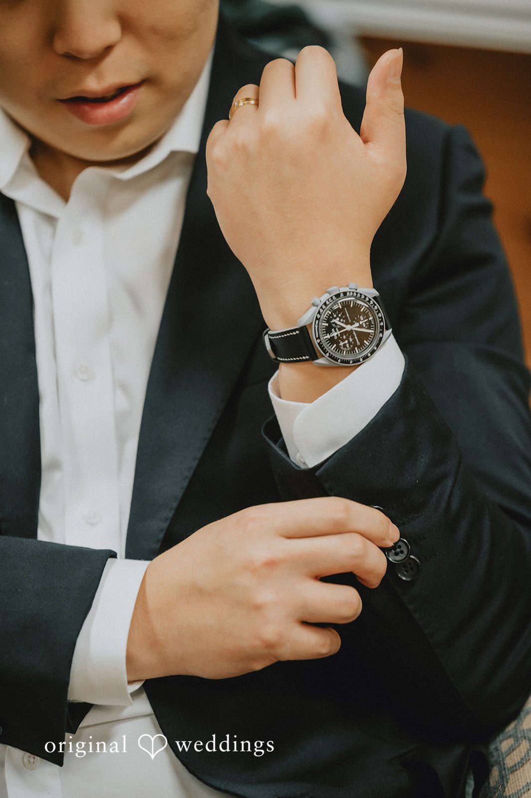 Sean + Hannah A close-up shot of a man wearing a black suit jacket while adjusting his wristwatch.