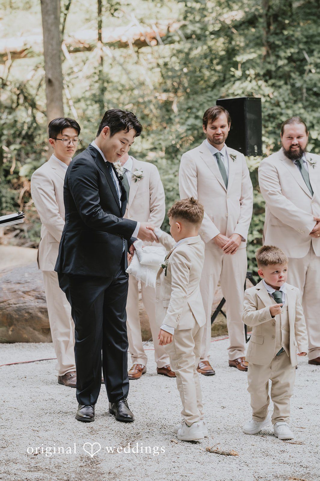 Sean + Hannah A group of groomsmen in light-colored suits pose together next to a rocky cliff.
