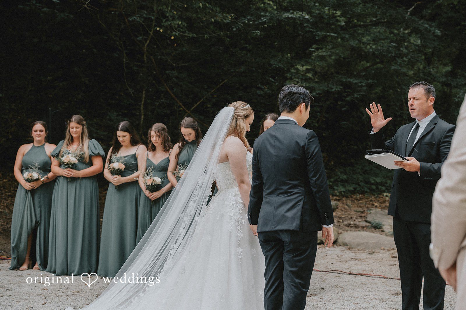 Sean + Hannah A bride and groom stand before an officiant during a ceremony next to a waterfall.