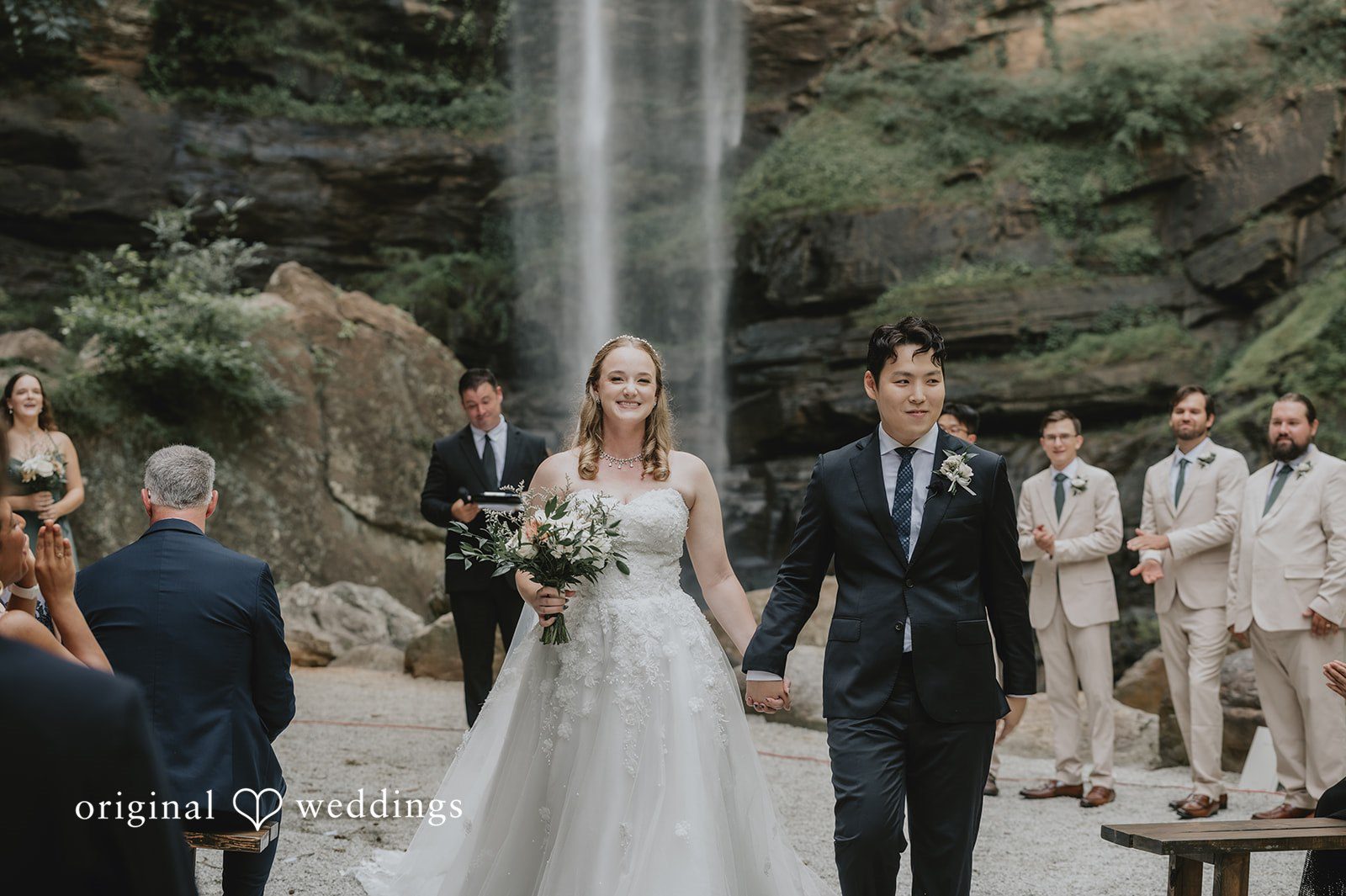 Sean + Hannah A bride and groom walk hand-in-hand past wedding guests after their ceremony.