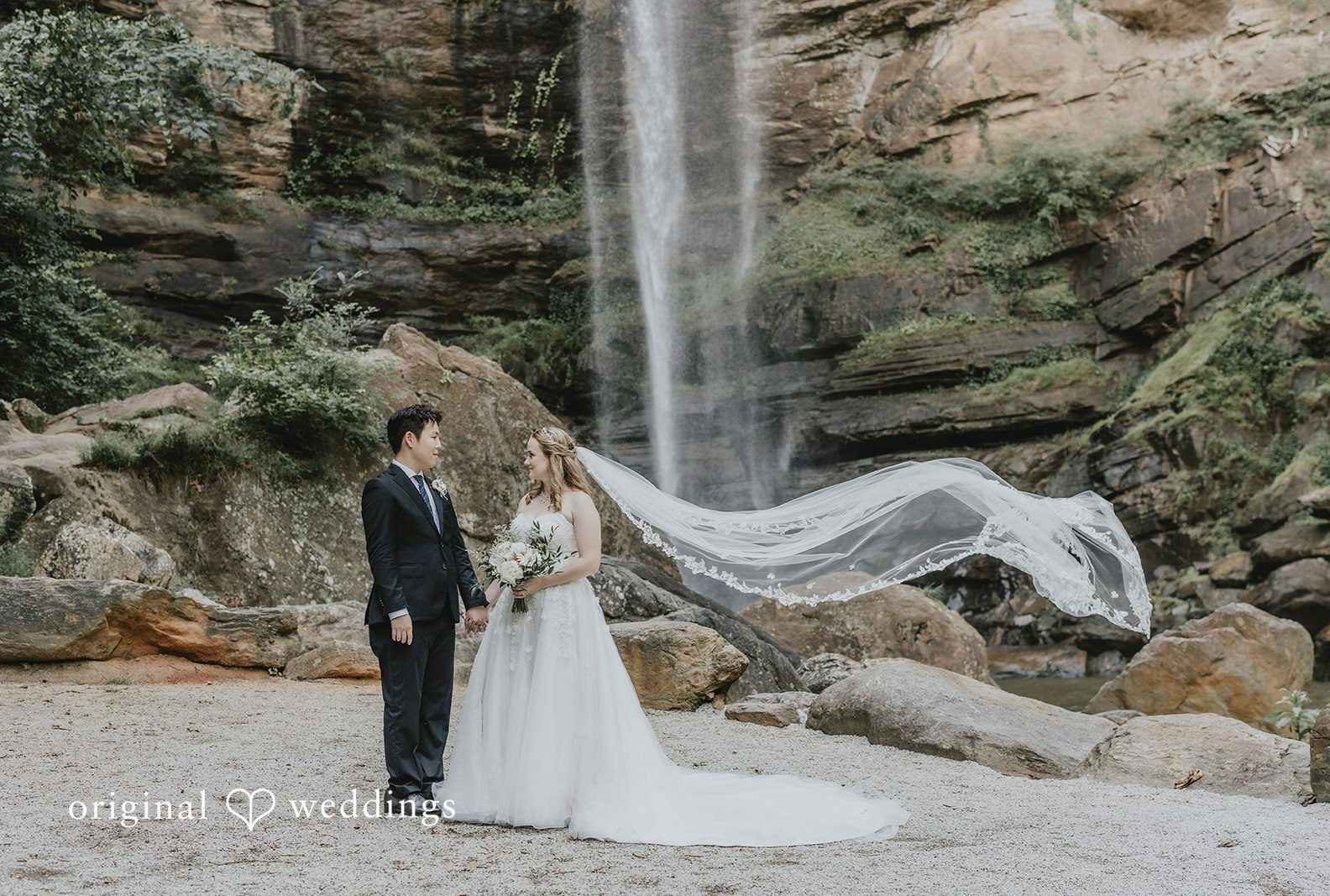 Bride and groom standing at the base of the waterfall, captured by Atlanta wedding photographers from Original Weddings at Toccoa Falls