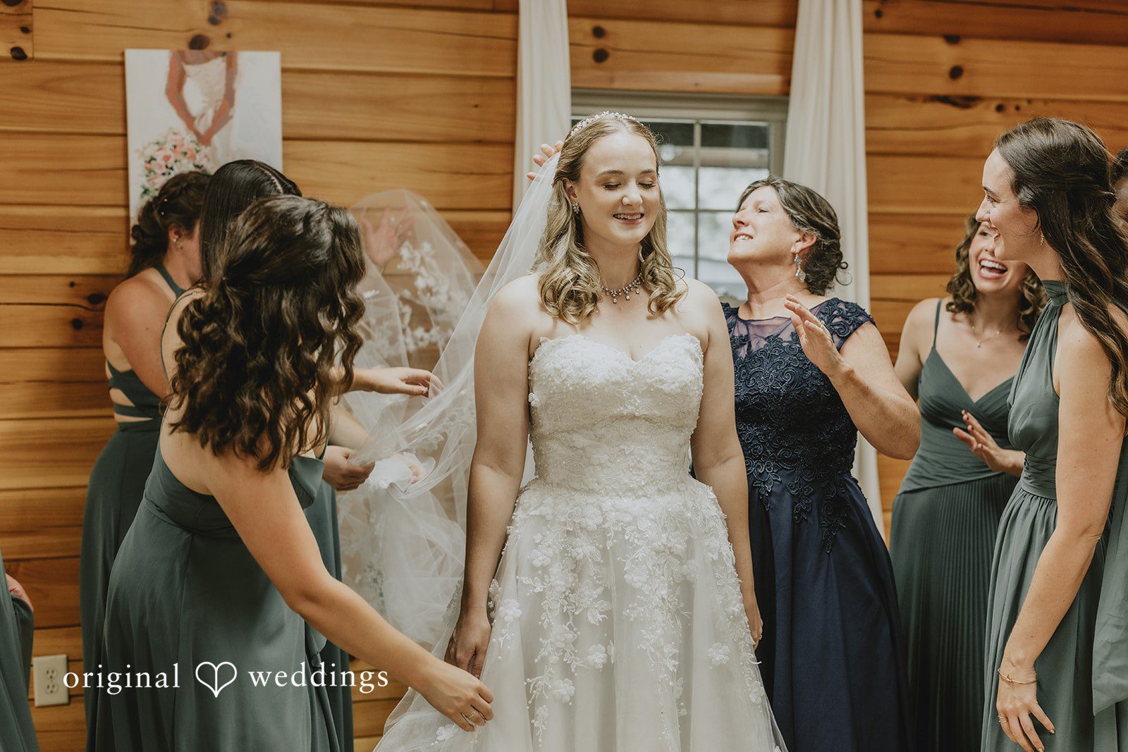 Sean + Hannah A group of bridesmaids in dark grey gowns gather around a bride in a white dress.