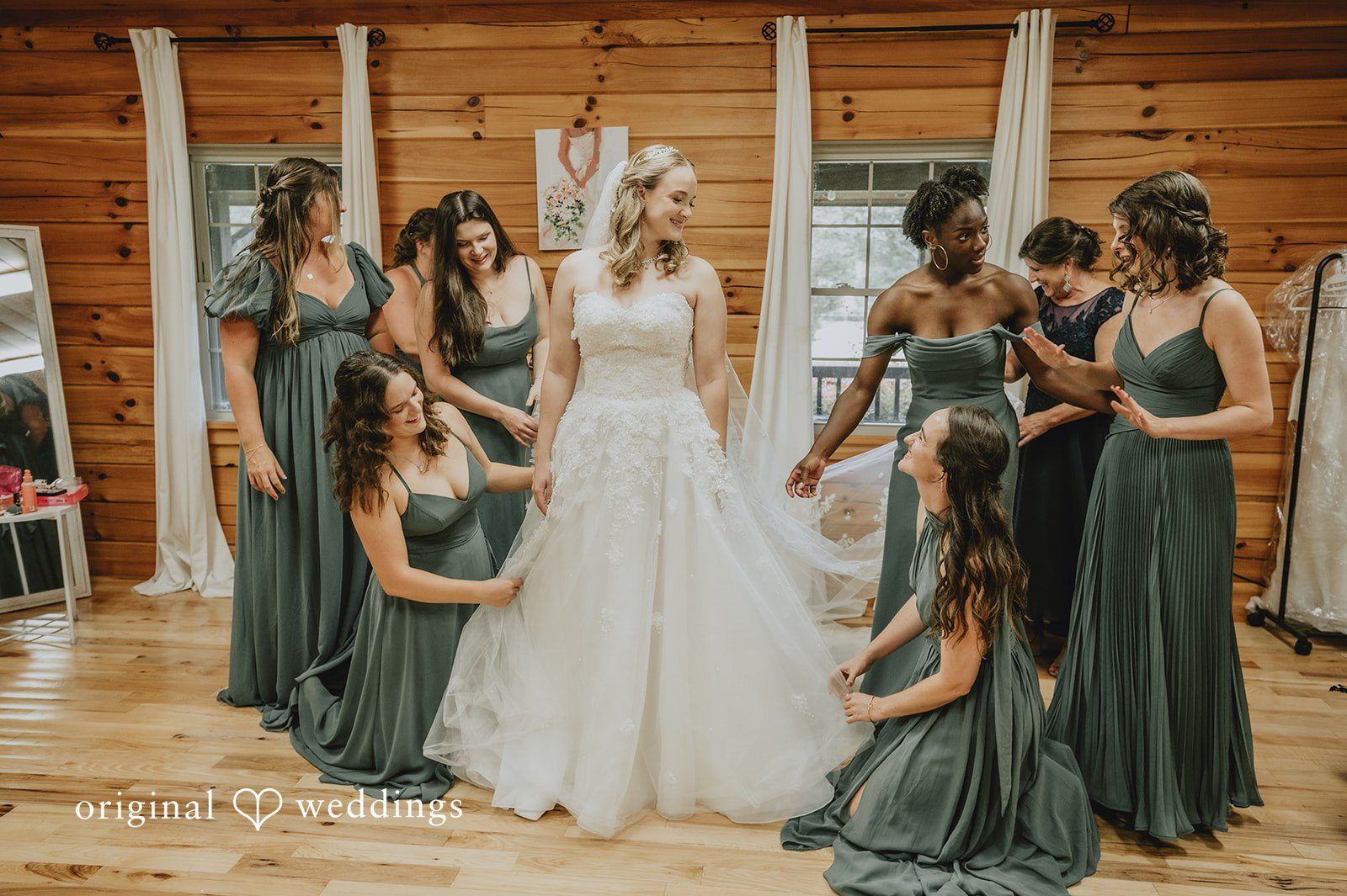 Sean + Hannah A group of bridesmaids in dark olive gowns stand in a circle around a bride.