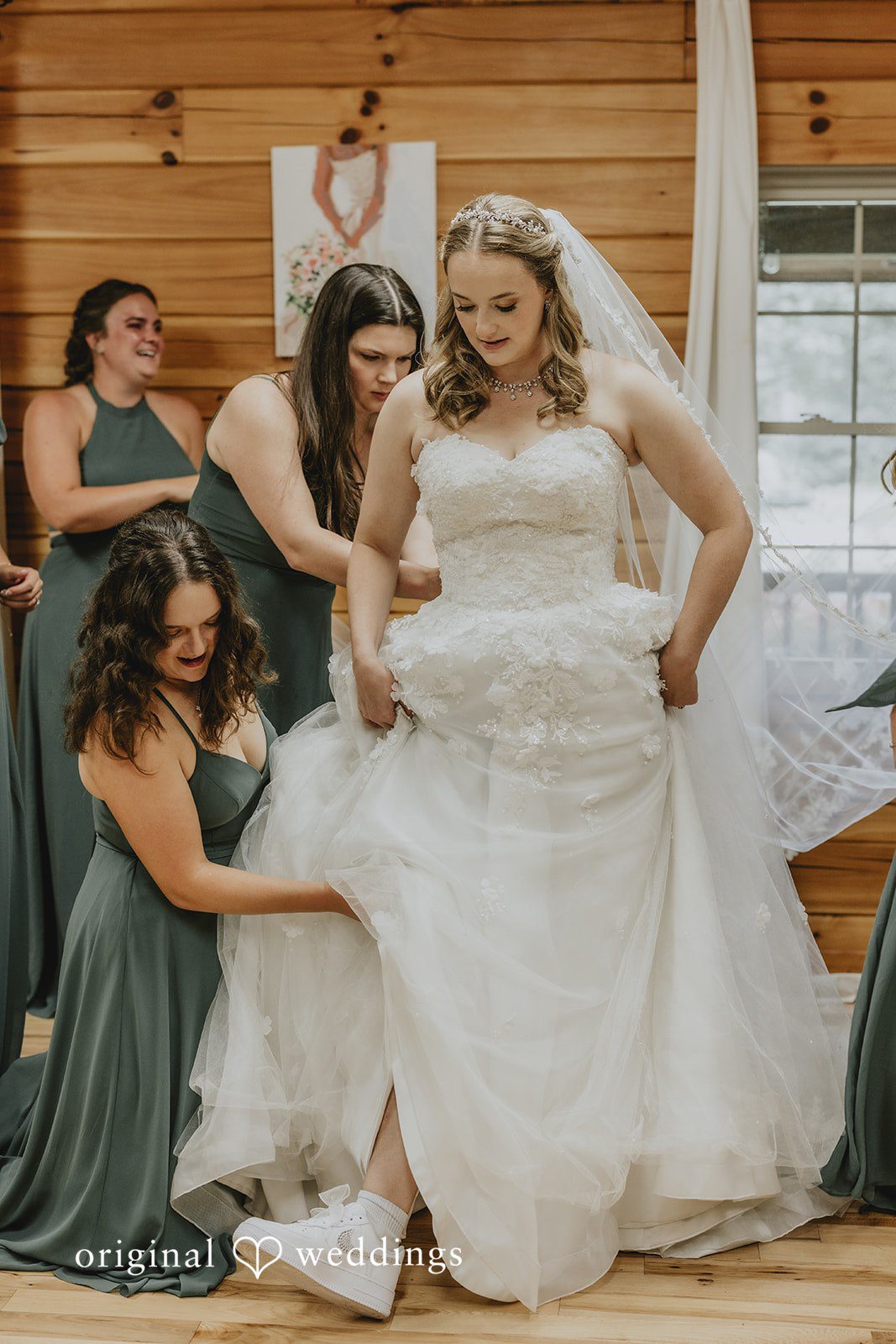 Sean + Hannah A bride stands with bridesmaids inside a wood-paneled room as they help her prepare.