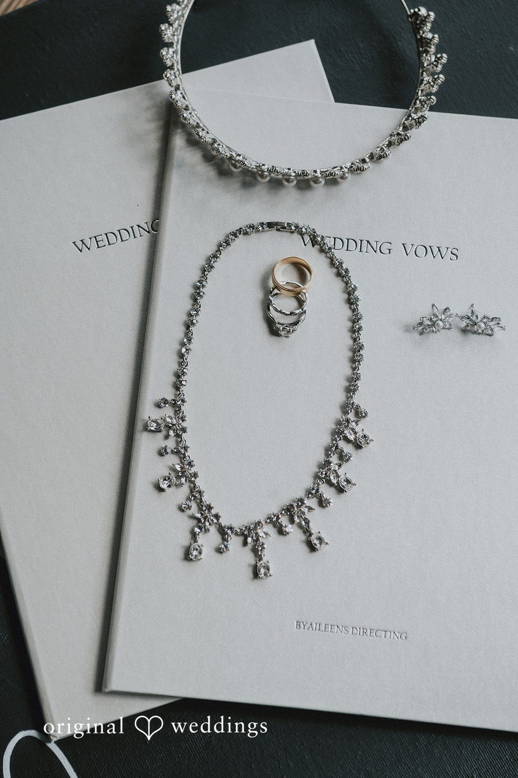 Sean + Hannah A flat lay display of wedding invitations, a beaded necklace, and a ring.
