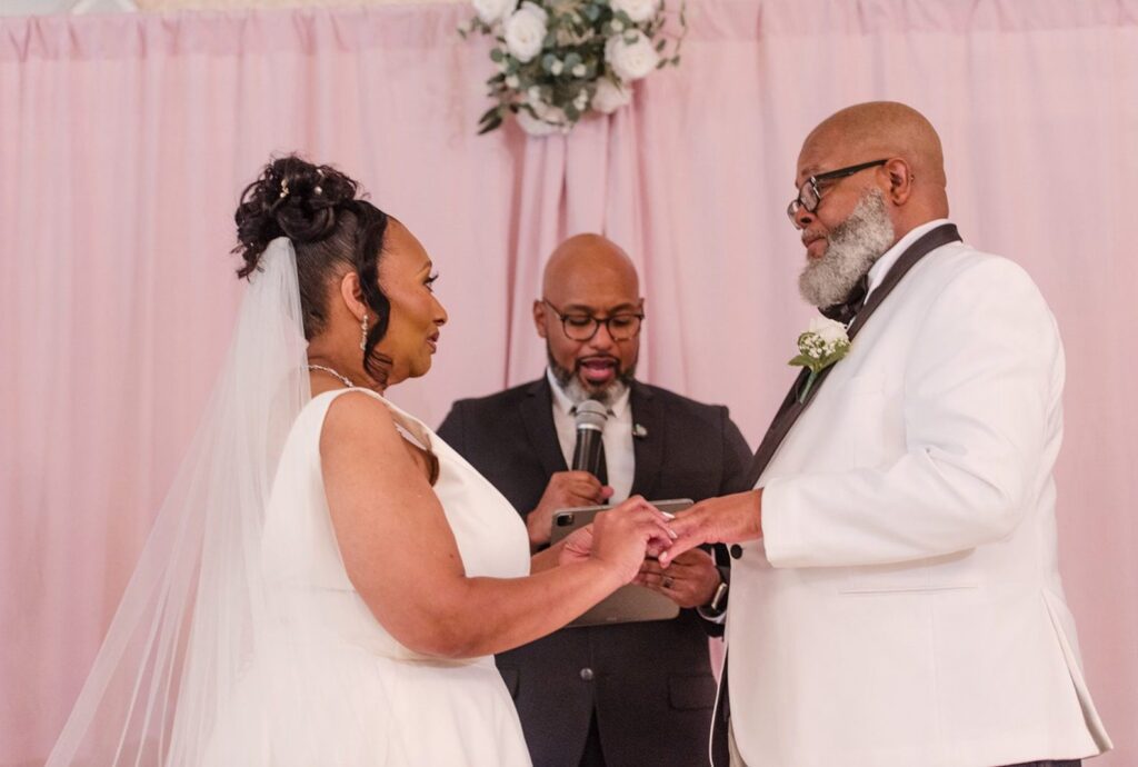 Tom's Country Place Wedding | Theodore & Kimberle 1 Theodore and Kimberle exchanging rings in front of a pink draped backdrop, captured by Cleveland wedding photographers from Original Weddings at Tom's Country Place