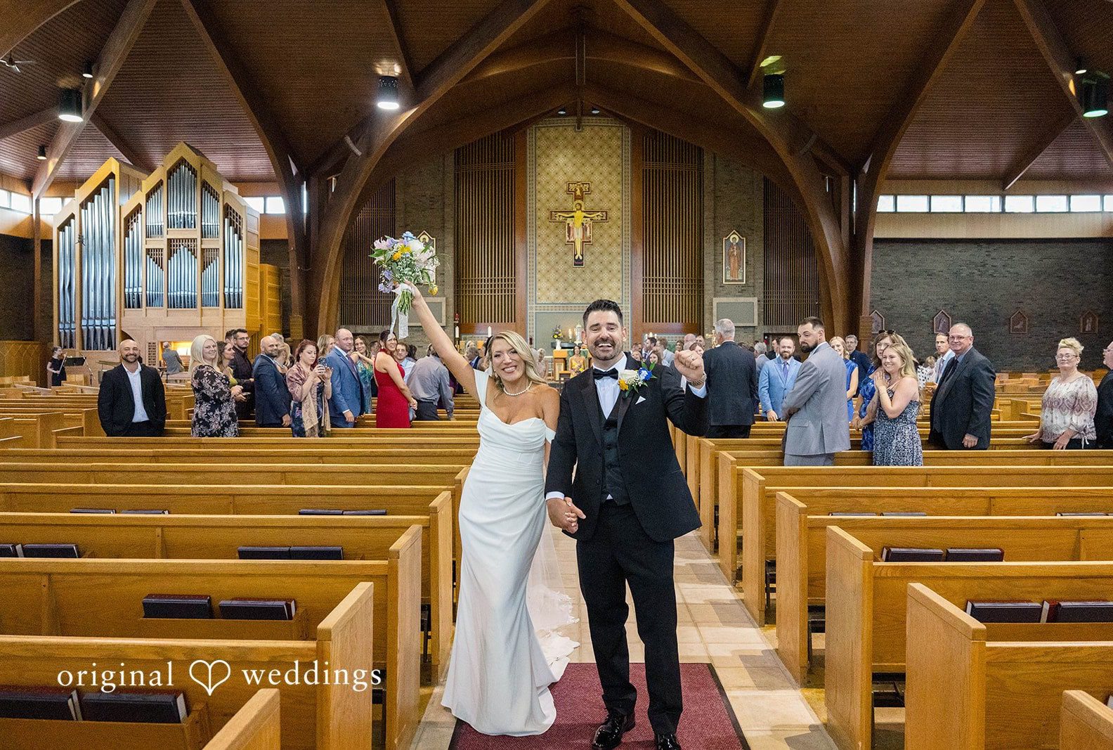 Newlyweds cheering as they walk up the church aisle, captured by Detroit wedding photographers from Original Weddings at Vinology