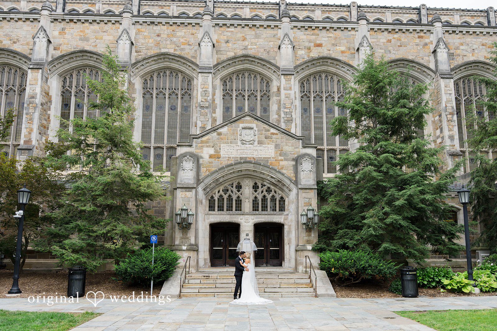 Stone building entrance with the bride and groom on the lawn path