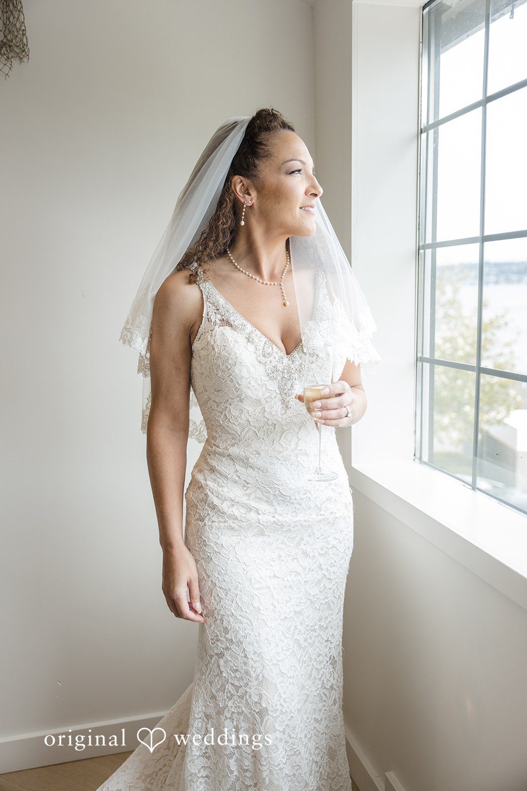Jennifer + Tony A smiling bride in a white gown and veil looking out a bright window.
