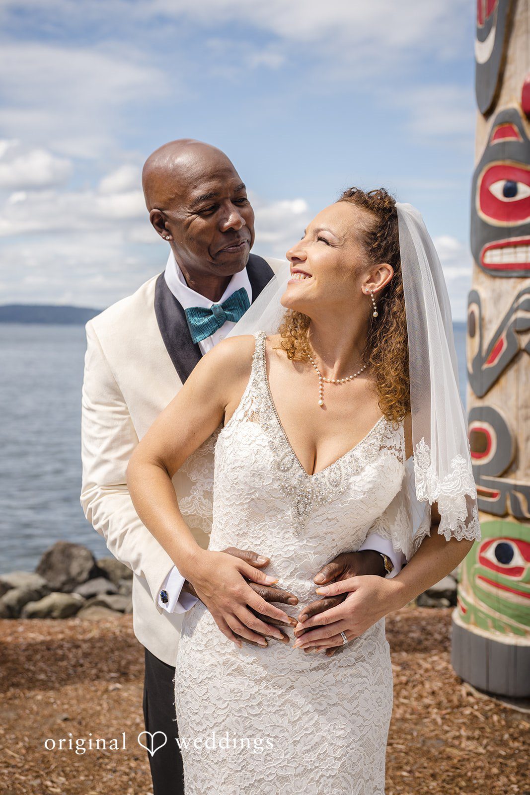 Jennifer + Tony A bride and groom laughing together while posing near a rustic wooden totem pole.