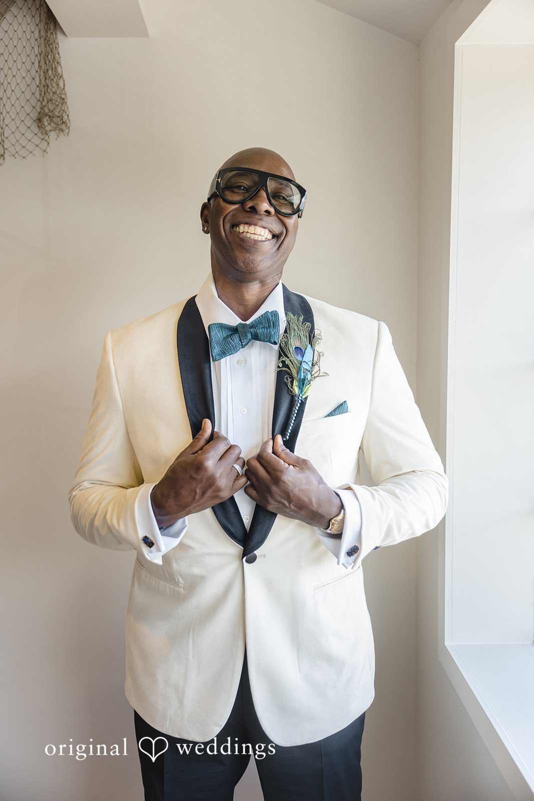 Jennifer + Tony A groom wearing a white tuxedo jacket, black bow tie, and glasses smiling.