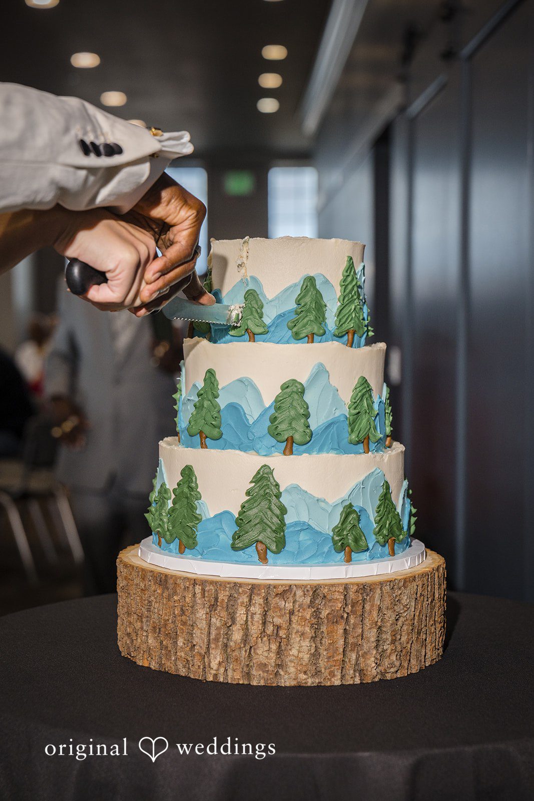 Jennifer + Tony A four-tier wedding cake decorated with green pine trees on a wooden slice base.