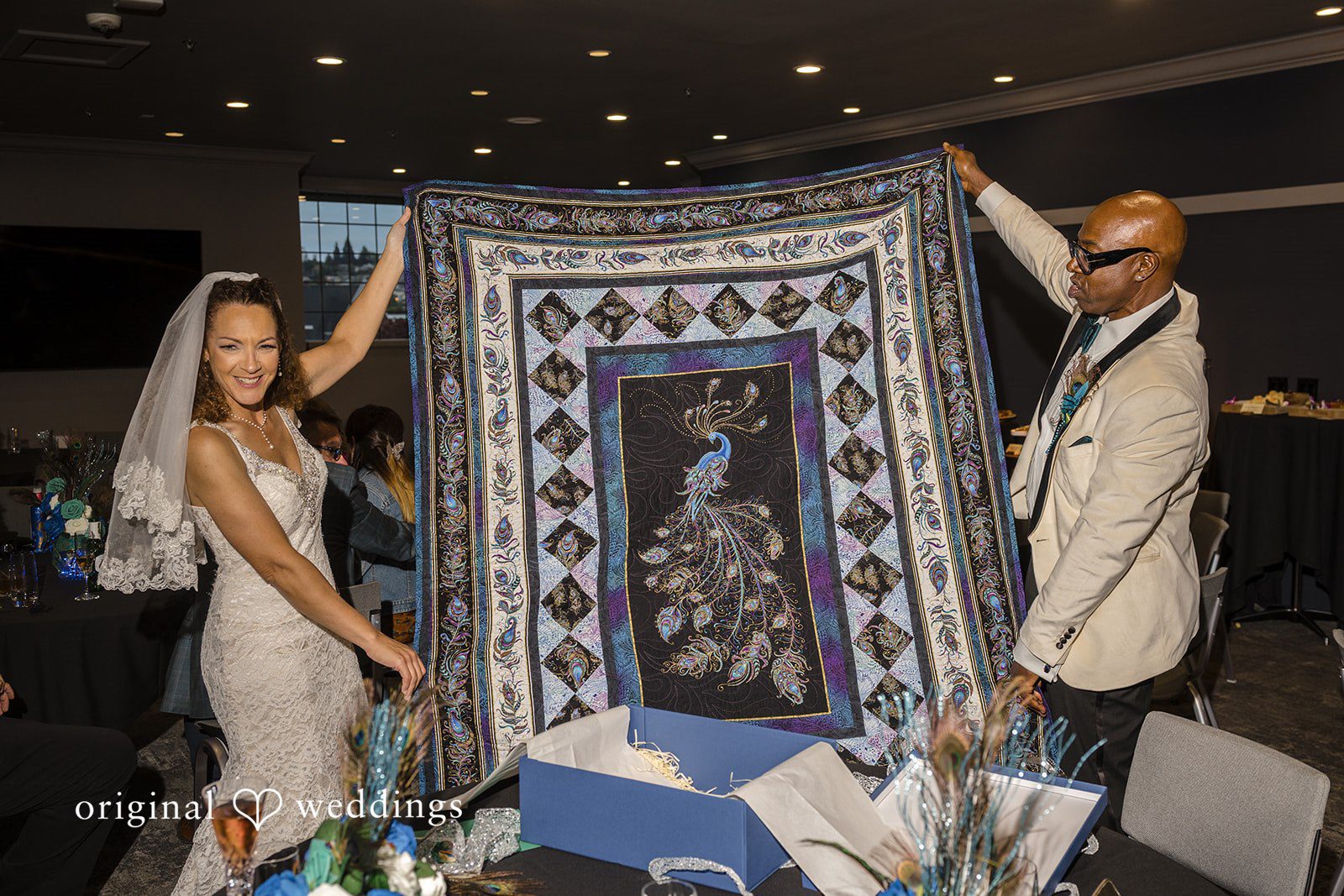 Jennifer + Tony A bride and groom holding up a large blue and white patterned quilt during their reception.